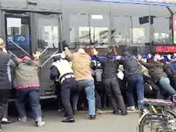 Heave ... Passers-by heed a call to help and begin to lift the bus off the trapped man. Picture: CCTV+ / YouTube