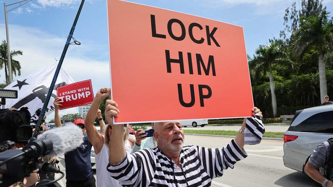 An anti-Trump demonstrator walks past supporters of former President Donald Trump as they wait for him to arrive at the Trump National Doral Miami resort.