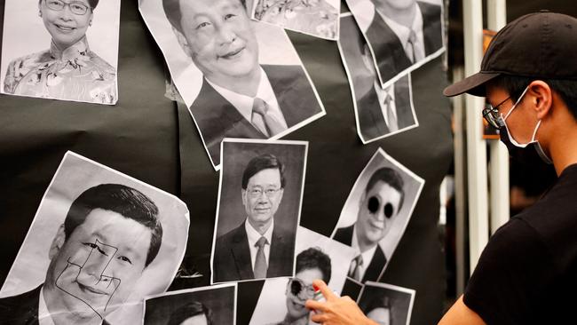 An activist sprays paint on portraits depicting Chinese President Xi Jinping, former Hong Kong chief executive Carrie Lam and current chief executive John Lee in Taipei. Picture: AFP