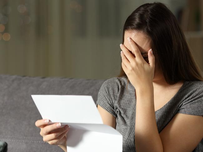 Sad woman reading a letter in the dark at home, renter, tenant, eviction, bill, stress, anxiety - for Herald Sun realestate