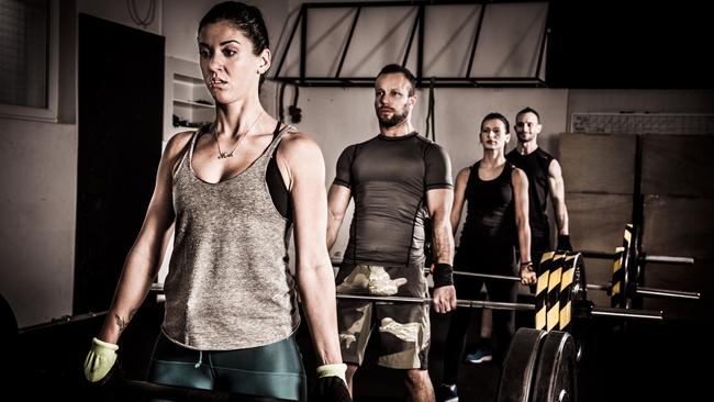 Group of young people lifting weights on a cross training in the gym. They are doing deadlift. All men and women are in their early thirties. They were placed in a line one behind the other. (The girl in the foreground has a necklace with her name)