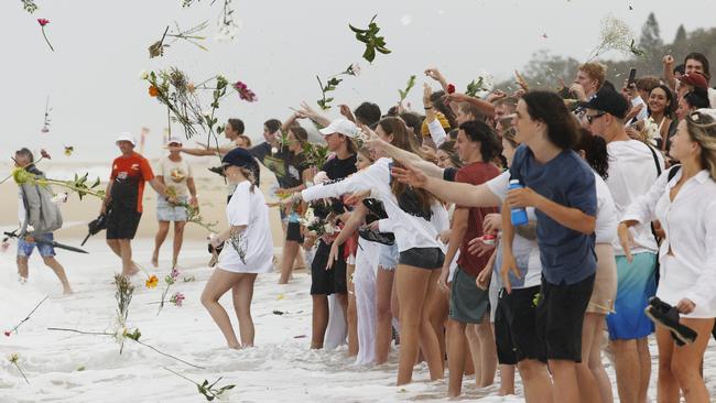 Family and friends of Balin Stewart throw flowers in tribute on his home beach at Buddina. Picture: Lachie Millard