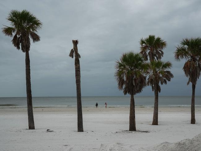 A decapitated palm is seen as a couple walks along the beach in Clearwater, Florida ahead of Hurricane Milton's expected mid-week landfall. Winds are predicted to be 200km/h. Picture: AFP