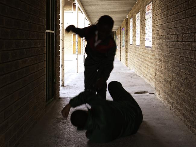 Two school kids fight in a dark passageway of their school, almost silhouette.