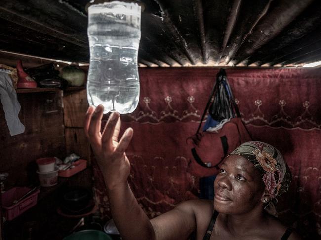 TOPSHOT - A resident looks at the light beaming from a freshly installed Amandla Elanga bottle globe inside her shack in an informal settlement in Olievenhoutbosch, Centurion, on February 6, 2023. The bottle globe provides day light from a two litre plastic bottle installed onto the roof of a shack by reflecting light from the sun: it contains a solution of water and and household bleach which also disinfects the water. - Scheduled blackouts, known as loadshedding, have burdened Africa's most industrialised economy for years, with its state-owned energy firm Eskom failing to keep pace with demand and maintain its ageing coal power infrastructure. (Photo by AFP)