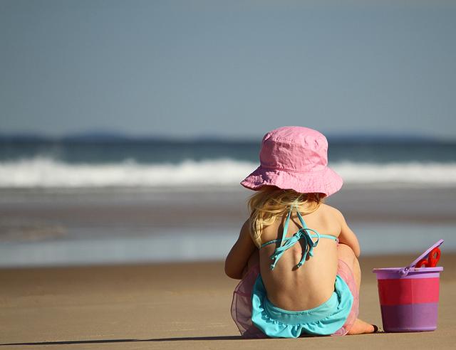 Little girl sitting at the beach with a bucket