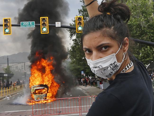 A protester looks on as a flipped over police vehicle burns in Salt Lake City. Picture: Rick Bowmer