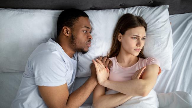 Sexual apathy concept. African American guy touching his upset girlfriend in bed, woman refusing him, top view. Young black couple having difficulties in sex, suffering from relationship problems