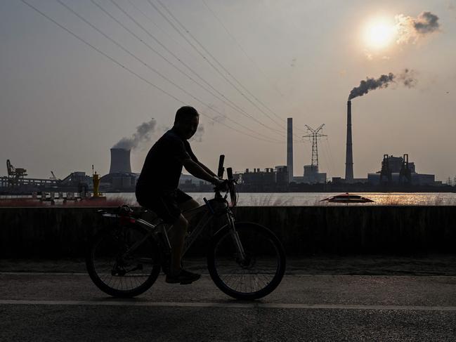 A man rides a bike across the river from Shanghai’s Wujing coal power station. Picture: Hector Retamal/AFP