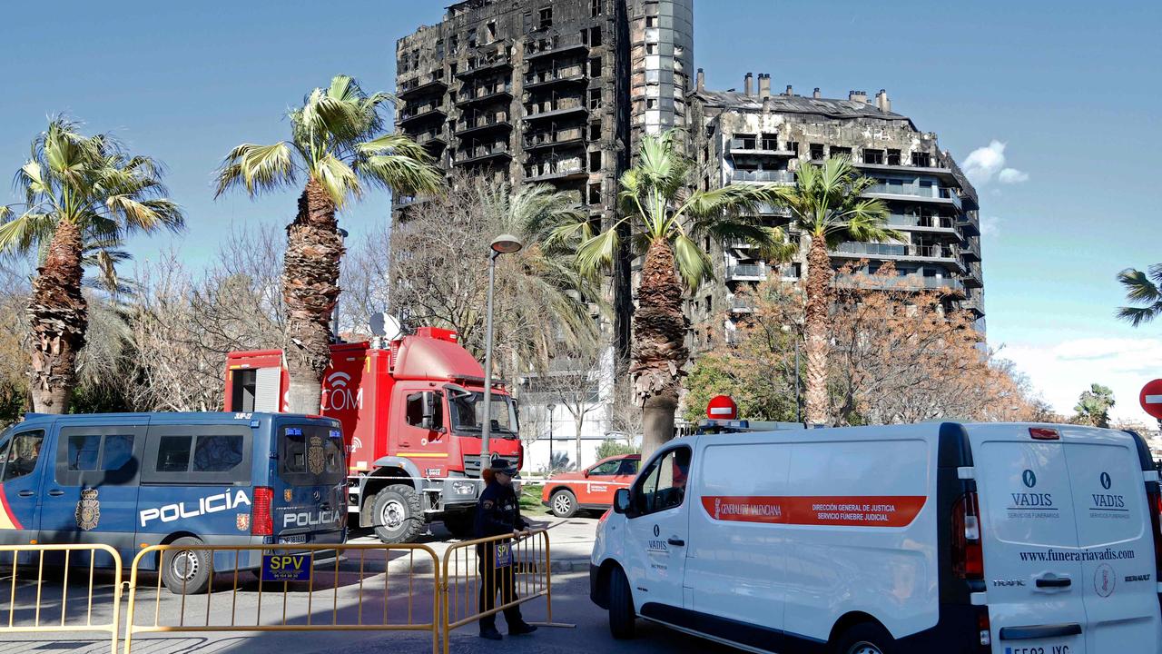 A police officer allows passage to a mortuary van at the multistorey residential block ravaged yesterday by a huge fire in Valencia on February 23, 2024. (Photo by JOSE JORDAN / AFP)