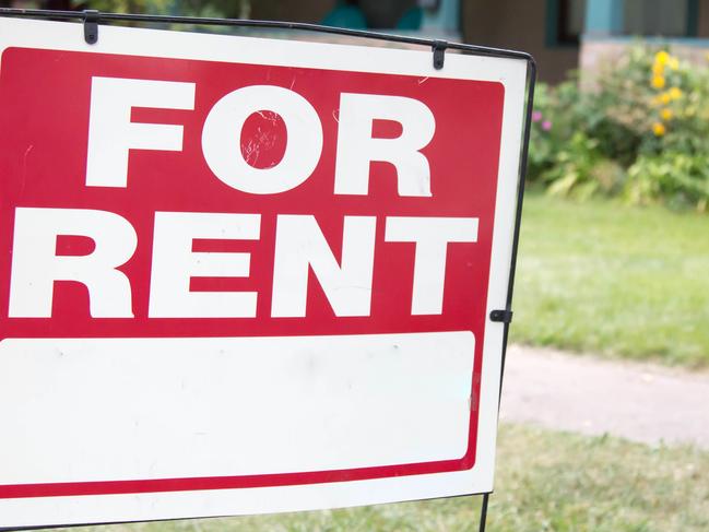 A blank red and white for rent sign is posted in the front yard of a home. The home has a porch and is a rental property.