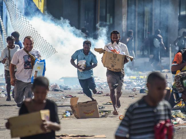 TOPSHOT - People run with merchandise as crowds leave shops with looted goods amid a state of unrest in Port Moresby on January 10, 2024. A festering pay dispute involving Papua New Guinea's security forces on January 10 sparked angry protests in the capital, where a crowd torched a police car outside the prime minister's office. By Wednesday afternoon pockets of unrest had spread through the capital Port Moresby, with video clips on social media showing crowds looting shops and stretched police scrambling to restore order. (Photo by AFP)