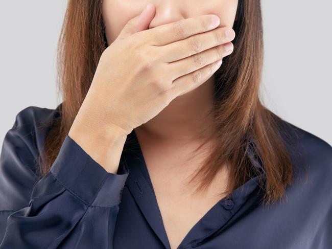 The woman in a dark blue shirt not commenting and refusing. woman with her hands on her mouth because of bad breath or halitosis