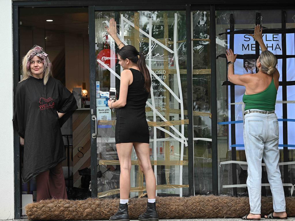 Hair customer Georgie Buckton looks on as hair salon worker Mikayla Gushal and salon owner Susanne Nicholson tape and protect windows at Thorneside, Brisbane. Picture: Lyndon Mechielsen/Courier Mail