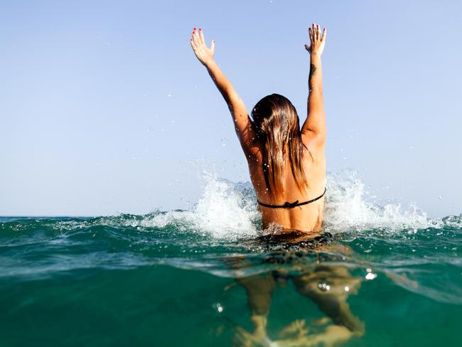 sexy bikini girl swim sea waves hands up jump splash in tropics on vacation back view