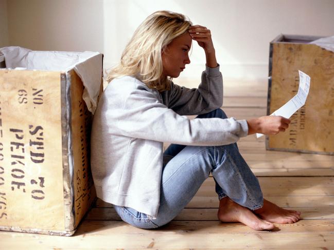 Undated. Generic picture of distraught woman sitting on bare floorboards holding credit card debt account bill while leaning against packing teachests crates boxes before moving house : GETTY IMAGES