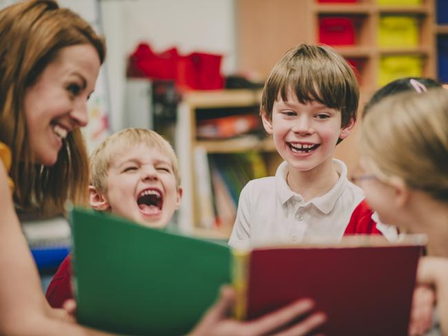 Teacher is sitting in the classroom with her primary school students, reading a story to them.