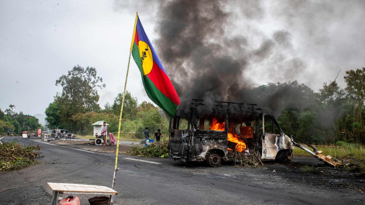 TOPSHOT - This photograph shows a Kanak flag waving next to a burning vehicle at an independantist roadblock at La Tamoa, in the commune of Paita, France's Pacific territory of New Caledonia on May 19, 2024. French forces smashed through about 60 road blocks to clear the way from conflict-stricken New Caledonia's capital to the airport but have still not reopened the route, a top government official said on May 19, 2024. (Photo by Delphine Mayeur / AFP)
