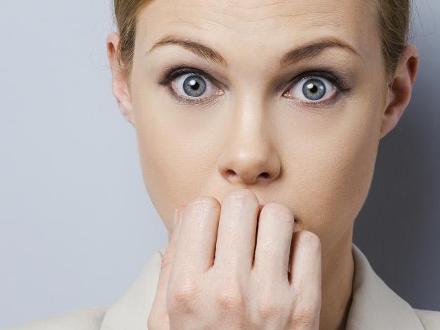 A little bit nervous. Nervous young businesswoman biting her nails while standing against grey background