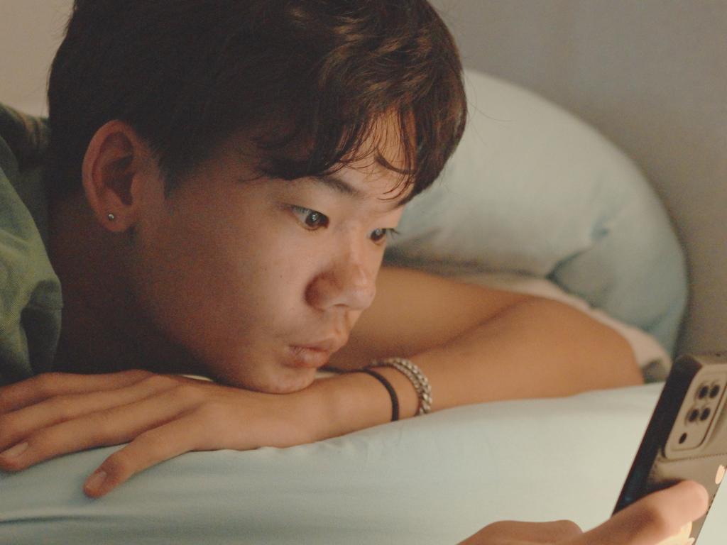 Mixed Asian teenage boy lying on bed with smartphone, anxiety and depression in adolescence, mental health awareness month, social media addiction and cyberbullying concept