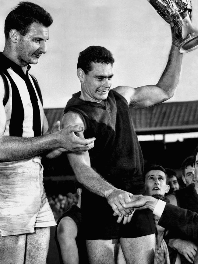 Ron Barassi accepts the premiership cup in 1964 with Collingwood’s Ray Gabelich looking on.