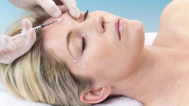 Woman lying down receiving botox injection in her forehead.