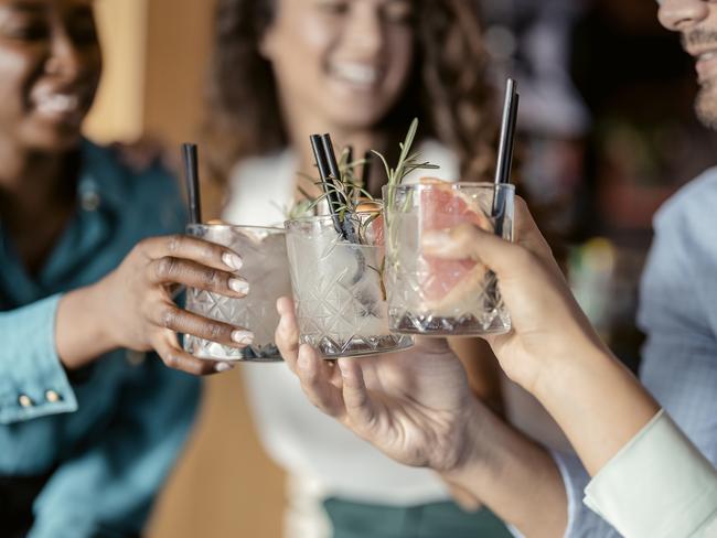 People with alcohol drinks clinking glasses in a restaurant having fun together, laughing, drinking cocktails. Party, celebration, nightlife and people concept - smiling friends clinking glasses