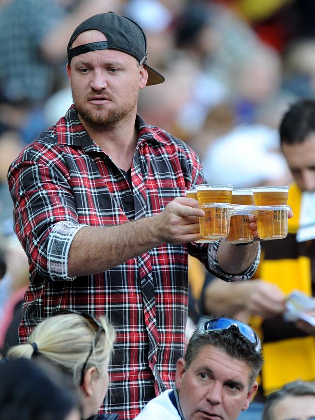 Every footy fan knows that squeezing through your row with a full tray of beers in plastic cups can be a perilous journey. Picture: AAP Image/Joe Castro