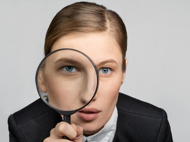 Portrait of a girl in the office at work looks carefully into the magnifying glass with one eye. The concept of office work and search. tax generic