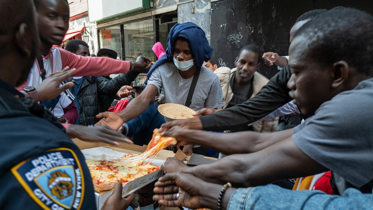 A police officer hands out pizza to dozens of recently arrived migrants to New York City as they camp outside of the Roosevelt Hotel. (Photo by SPENCER PLATT / GETTY IMAGES NORTH AMERICA / Getty Images via AFP)