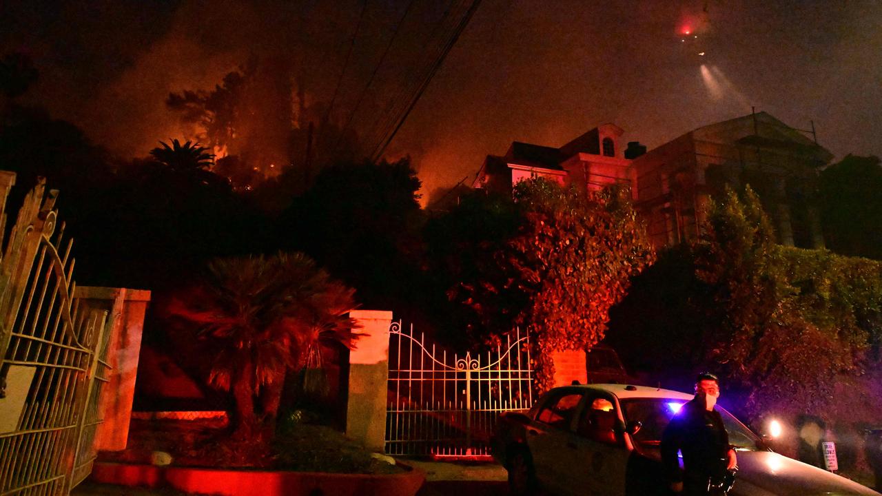 A police officer stands below burning brush at the Sunset Fire near Hollywood Blvd in the Hollywood Hills. Picture: Robyn Beck / AFP