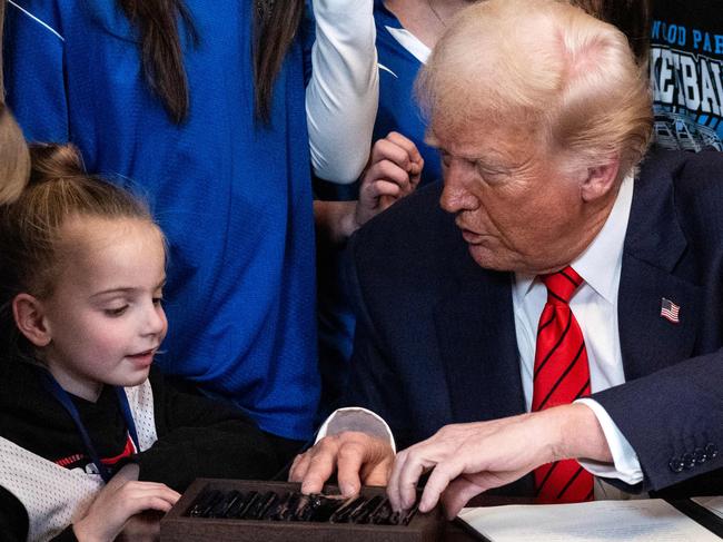 US President Donald Trump speaks with a little girl as he selects a pen to sign the No Men in Women's Sports Executive Order in the East Room of the White House in Washington, DC, on February 5, 2025. President Trump on Wednesday is signing an executive order to ban transgender girls and women from competing on sports teams that match their gender identity, marking his latest move targeting transgender rights. (Photo by ANDREW CABALLERO-REYNOLDS / AFP)