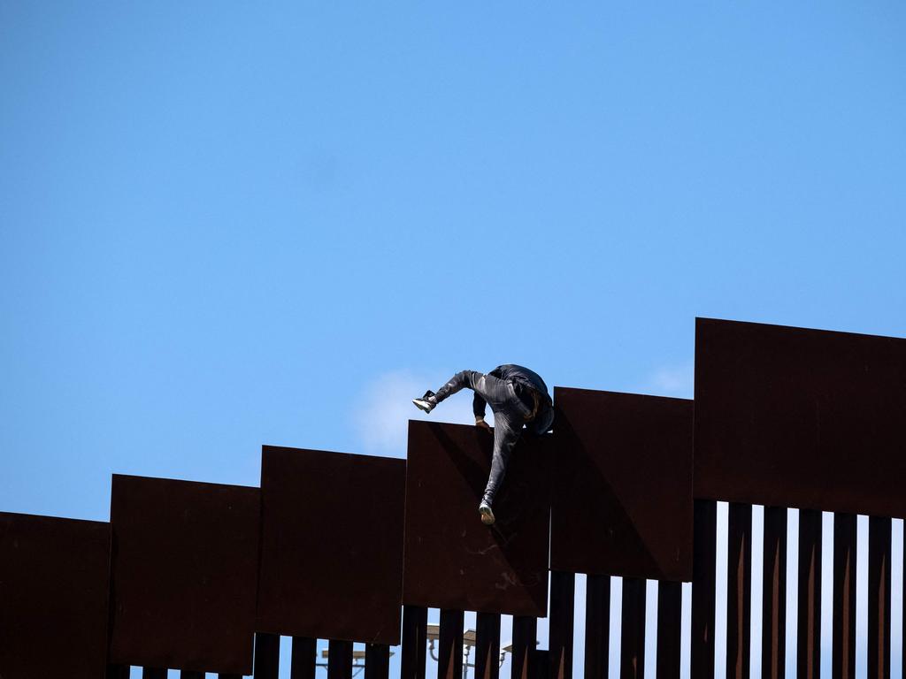 A migrant climbs over the border fence into the United States after fetching groceries for other migrants waiting to be processed by authorities on the US side of the US-Mexico border.