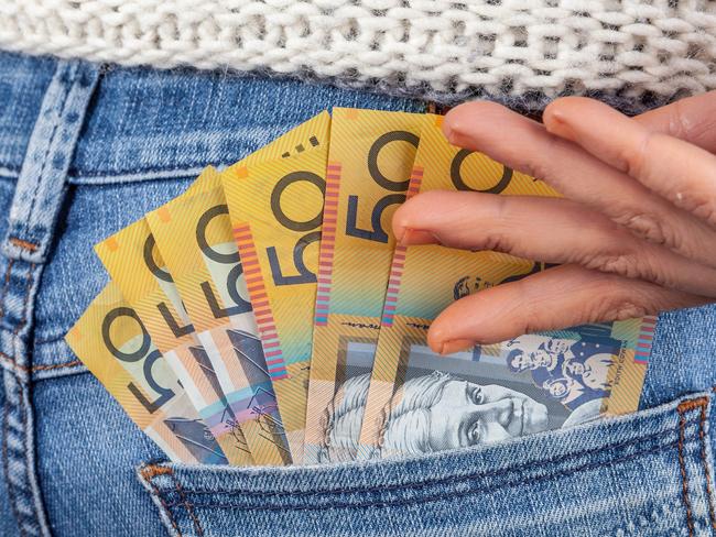 Female hand reaching for 50 Australian dollar bills in her jeans back pocket