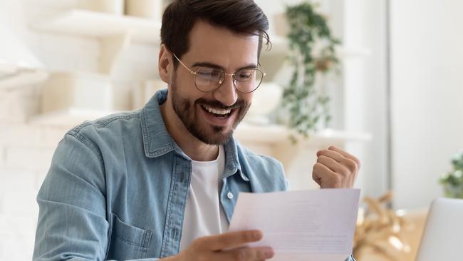 Head shot happy young man winner in eyeglasses reading paper letter with good news, making yes gesture. Joyful bearded guy celebrating personal achievement or banking loan approval, taxes refund.