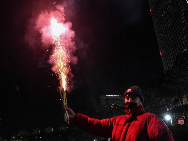 A man holds a firecrackes to celebrate the New Year out the Lotte World Tower skyscraper in Seoul on January 1, 2022. Picture: Jung Yeon-je / AFP.