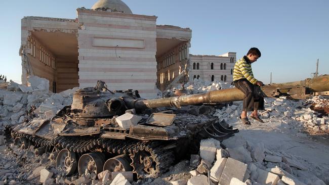 A boy plays on the gun of a destroyed Syrian army tank north of the restive city of Aleppo. Picture: AFP