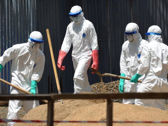 Health workers from the Liberian Red Cross wear protective gear as they shovel sand which will be used to absorb fluids emitted from the bodies of Ebola victims in Monrovia. AFP PHOTO / ZOOM DOSSO