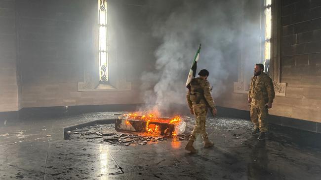 Rebel fighters stand next to the burning gravesite of Bashar al-Assad’s father, Hafez al-Assad at his mausoleum in the family's ancestral village of Qardaha. Picture: AFP