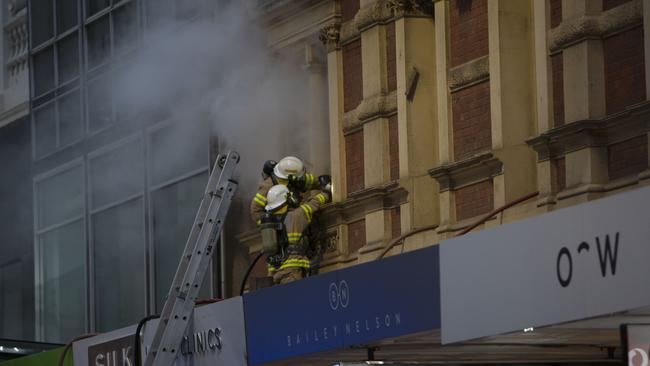 Members of the SA Metropolitan Fire Service climb through a window as toxic smoke billows from a heritage building on Rundle Mal. Picture: AAP/Emma Brasier