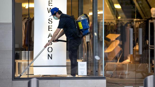 A masked worker cleans inside a shop window in Melbourne’s Bourke St. Picture: NCA NewsWire / David Geraghty