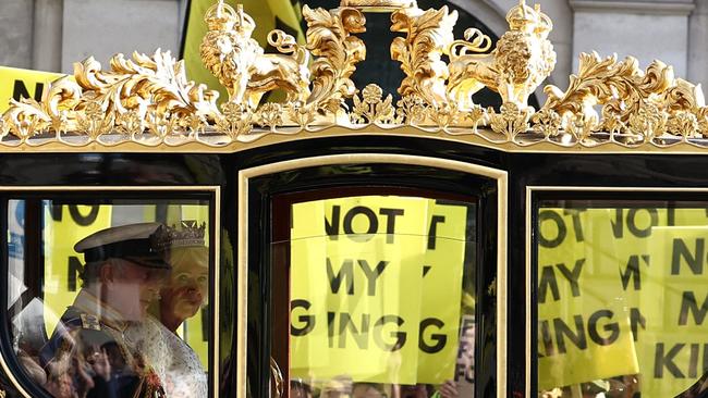 TOPSHOT - Britain's King Charles III and Britain's Queen Camilla travel in the Diamond Jubilee State Coach past protesters holding 