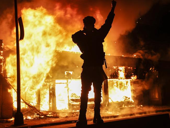 A demonstrator stands beside a fire of a building that was once a check cashing business/ Picture: John Minchillo