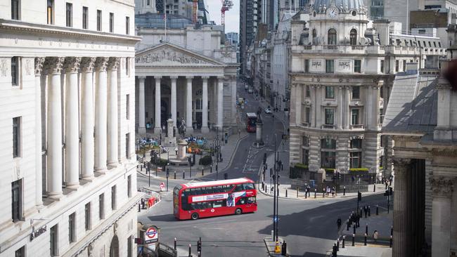 A double decker bus drives through the empty streets of the City of London.