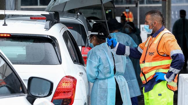 Healthcare workers check details of cars lined up at Darebin Arts Centre in Preston. Picture: Ian Currie