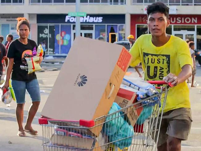 This screen grab from AFPTV video footage taken on January 10, 2024 shows people carrying items as crowds leave shops with looted goods amid a state of unrest in Port Moresby. A festering pay dispute involving Papua New Guinea's security forces on January 10 sparked angry protests in the capital, where a crowd torched a police car outside the prime minister's office. By Wednesday afternoon pockets of unrest had spread through the capital Port Moresby, with video clips on social media showing crowds looting shops and stretched police scrambling to restore order. (Photo by AFP)