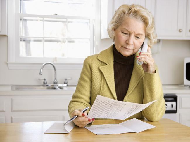 Generic image of an older woman talking on cordless phone at home looking at paperwork.