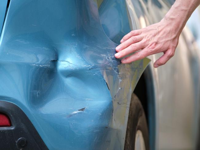 Driver hand examining dented car with damaged fender parked on city street side. Road safety and vehicle insurance concept.