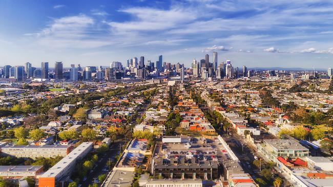 Aerial view of Melbourne city CBD high-rise towers from Port Melbourne and Southbank above residential suburb house roofs and local streets, roads, cars and parks.