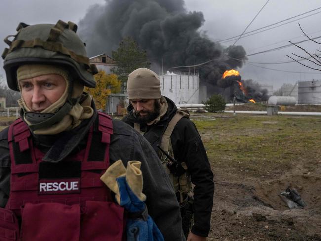 TOPSHOT - A Ukrainian rescue service member and a soldier inspect the area as black smoke rises from an oil reserve in Kherson on November 20, 2022, amid the Russian invasion of Ukraine. (Photo by BULENT KILIC / AFP)